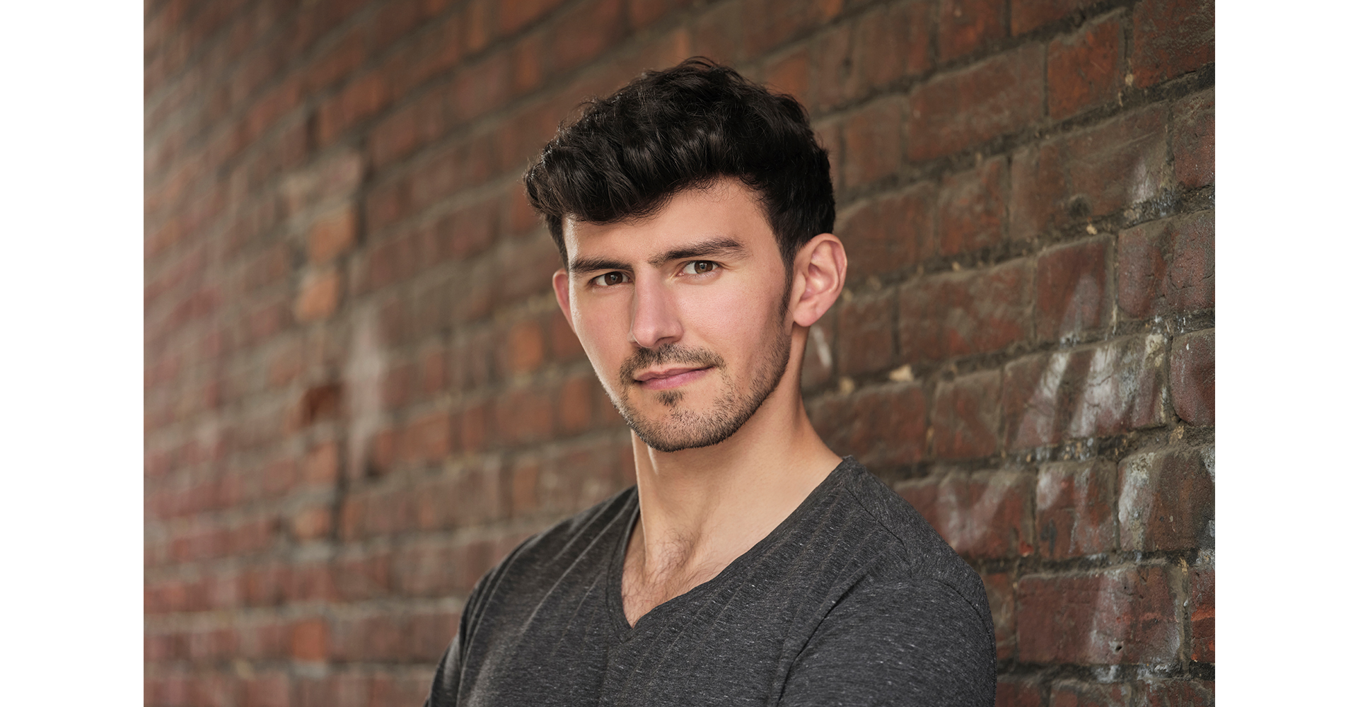 actor standing front brick wall in a grey top actor head shot natural light